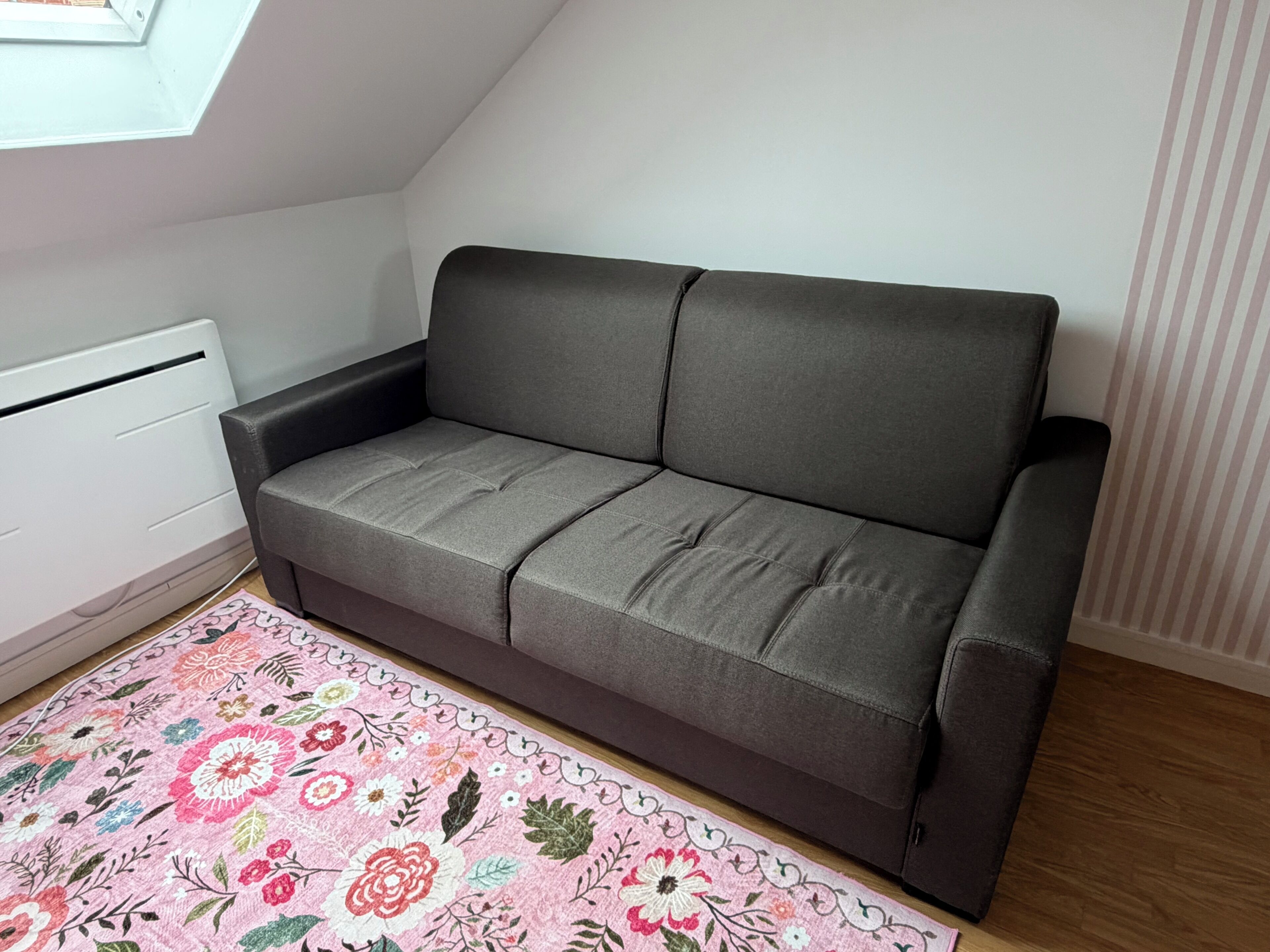 Un sofá gris en una habitación con suelo de madera, un radiador y una alfombra estampada.
