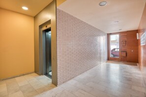 A hallway with a tiled floor, a brick wall, and a wooden door. - JULIA: Modern Apartment with Sea Views Next to Riells Beach (L'Escala)