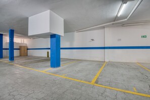 A parking garage with white walls, blue stripes, and yellow parking lines. - JULIA: Modern Apartment with Sea Views Next to Riells Beach (L'Escala)