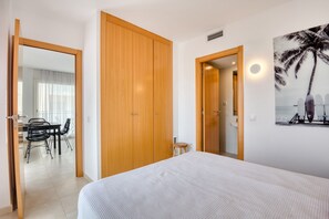 A hotel room with a bed, a wooden wardrobe, a dining area with chairs, and a view of the sea through the window. - JULIA: Modern Apartment with Sea Views Next to Riells Beach (L'Escala)