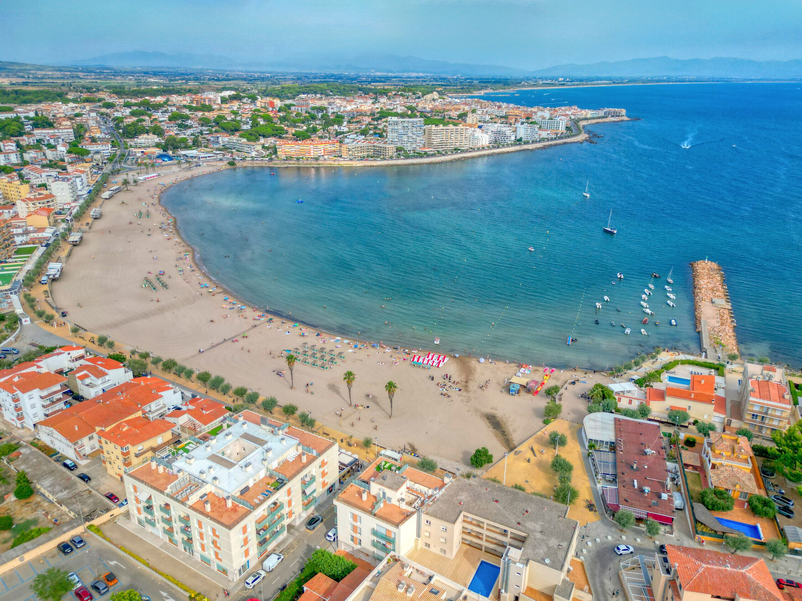 Vue aérienne d’une ville côtière avec une baie en forme de croissant, des bâtiments et une plage.