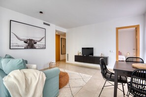 A modern living room with a sofa, a dining table with chairs, a TV on a cabinet, and a framed picture on the wall. - JULIA: Modern Apartment with Sea Views Next to Riells Beach (L'Escala)