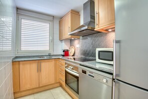 A modern kitchen with wooden cabinets, a stainless steel refrigerator, a microwave, and a built-in oven. - JULIA: Modern Apartment with Sea Views Next to Riells Beach (L'Escala)