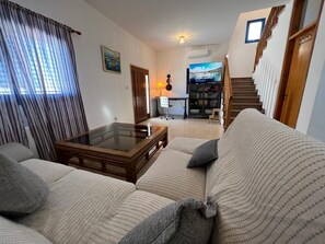 A living room with a sofa, a coffee table, a television, and a staircase leading to another level. - Jomavi Beach Eco-Villa (Polis Chrysochous)