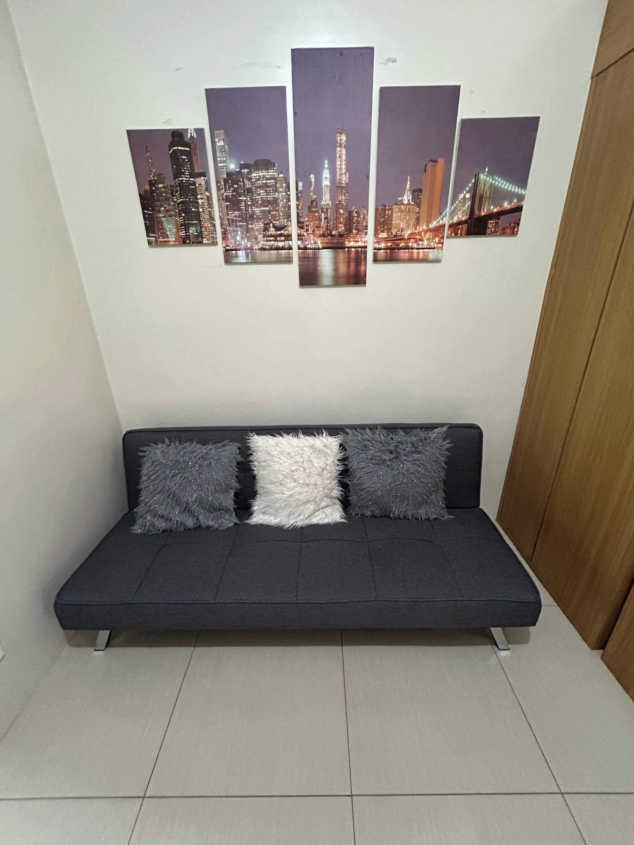 A dark-colored sofa with three fluffy pillows against a white wall.
