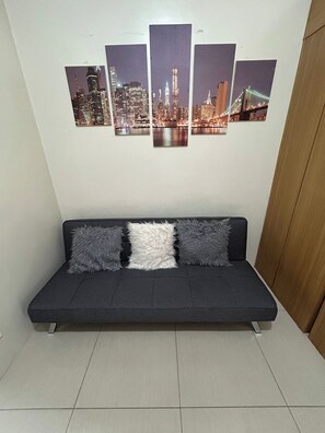 Un canapé de couleur sombre, agrémenté de trois coussins moelleux, est placé contre un mur blanc.