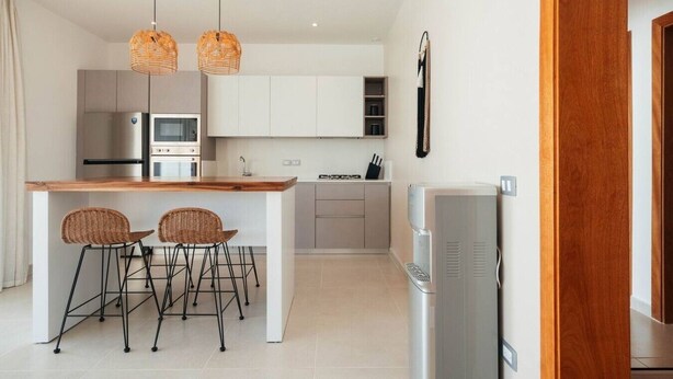 A modern kitchen with a central island, two wicker chairs, a refrigerator, and pendant lighting. - 2-Bed Ocean View on Beach • Sol de Arena C5 (Las Terrenas)