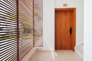 A wooden door with a number plate, a corridor with a slatted wall, and a tiled floor. - 2-Bed Ocean View on Beach • Sol de Arena C5 (Las Terrenas)