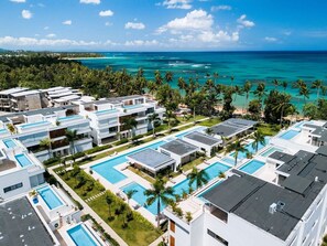 A resort with multiple swimming pools, modern architecture, and a view of the ocean. - 2-Bed Ocean View on Beach • Sol de Arena C5 (Las Terrenas)