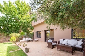 Eine Terrasse mit Gartenmöbeln, einem Topfpflanzen und einem Gebäude mit Schiebetür.