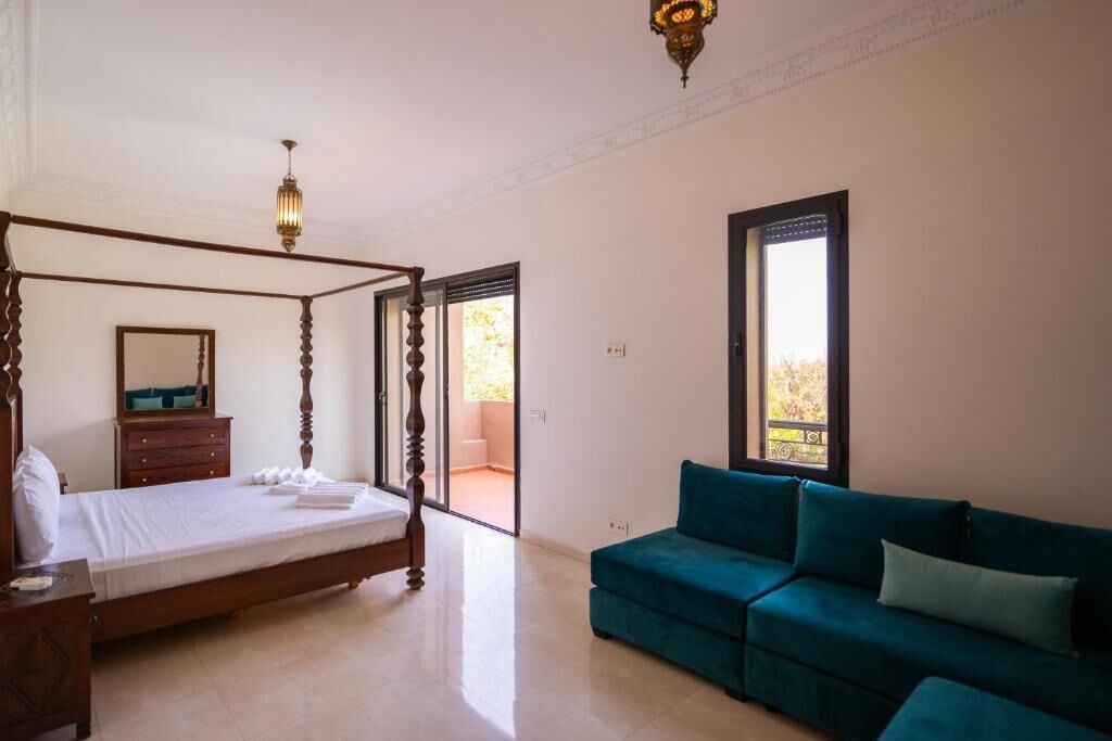 A bedroom with a four-poster bed, a dresser, a teal sofa, and a large window.