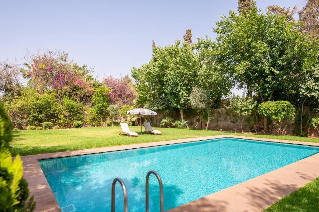 A rectangular swimming pool with two metal ladders, surrounded by a well-maintained lawn and various trees.