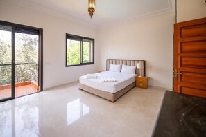 A bedroom with a bed, bedside table, and a view of greenery through a window. - Riad Garden Targa Pool (Marrakech)