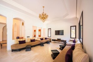 A spacious living area with a large sofa set, a flat-screen TV, and a chandelier. - Riad Garden Targa Pool (Marrakech)