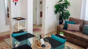 Un salon moderne avec une table basse en verre, un canapé marron agrémenté de coussins, une plante en pot et une petite table sur laquelle se trouvent une bouteille et des verres.