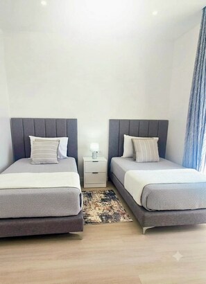 Ein Doppelzimmer mit zwei Betten, einem Nachttisch mit Lampe und einem gemusterten Teppich.