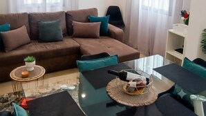 Un salon avec un canapé marron, des coussins turquoise, une table basse en verre et un téléviseur à écran plat fixé au mur.