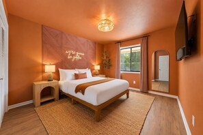 A bedroom with a bed, nightstands, a wall-mounted TV, and a large window with curtains. - Sleeps 14 ~ MiniGolf, HotTub, MovieRm, Sauna, Firepit (Columbus)