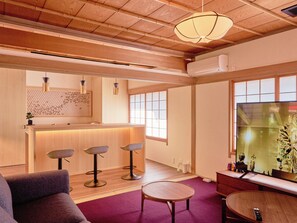 A modern interior with a wooden ceiling, a reception desk, bar stools, a round table, and a large window. - Imakusa-so, Nara, Naramachi - The Steam Bath House - (奈良市福智院町)