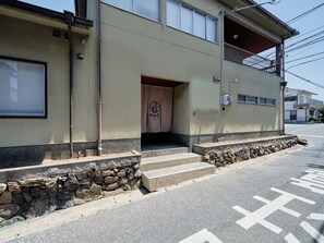 A building with a stone wall entrance, a visible door, and a small set of steps leading up to the entrance. - Imakusa-so, Nara, Naramachi - The Steam Bath House - (奈良市福智院町)