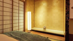 Ett traditionellt japanskt rum med tatamimattor på golvet, en shoji-skärm, ett lågt bord med en vas och en säng med ett grönt täcke.