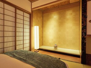 A traditional Japanese-style room with tatami flooring, a shoji screen, a low table with a vase, and a bed with a green blanket. - Imakusa-so, Nara, Naramachi - The Steam Bath House - (奈良市福智院町)