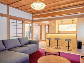 A modern interior with a sofa, stools, a wooden ceiling, and a sliding door. - Imakusa-so, Nara, Naramachi - The Steam Bath House - (奈良市福智院町)