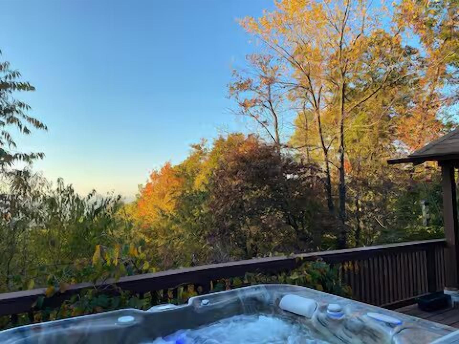 A hot tub on a wooden deck with a view of trees and a clear sky.