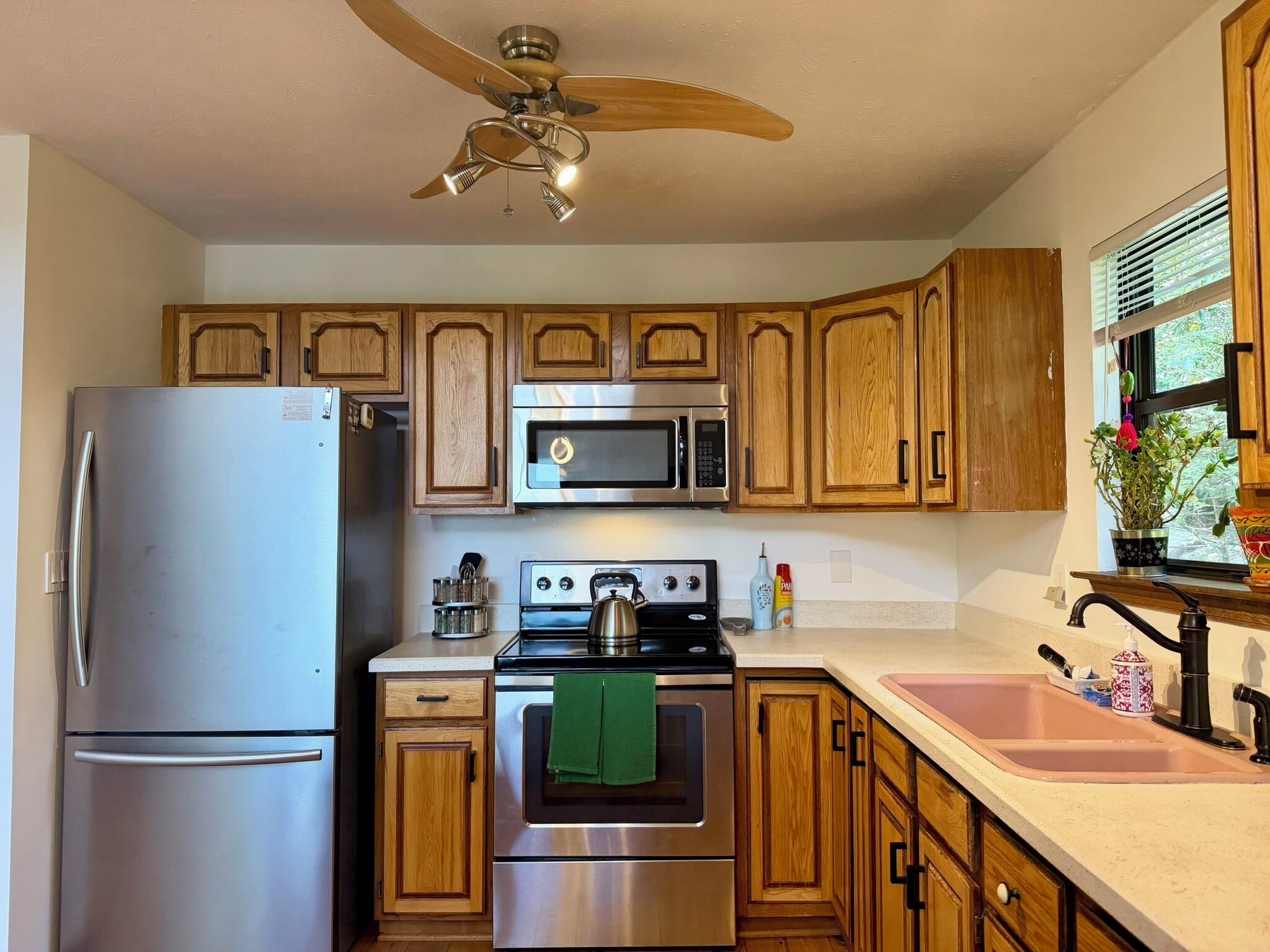 A kitchen with wooden cabinets, a stainless steel refrigerator, a microwave, an oven, a stove, and a ceiling fan.