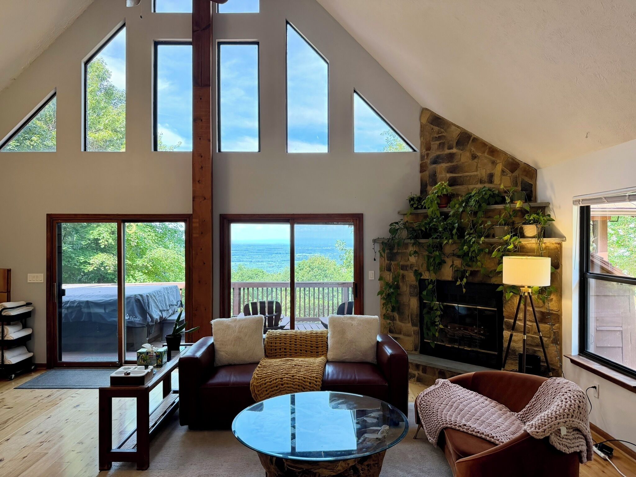 A spacious living room with a high ceiling, large windows, a fireplace, and a balcony with a view.