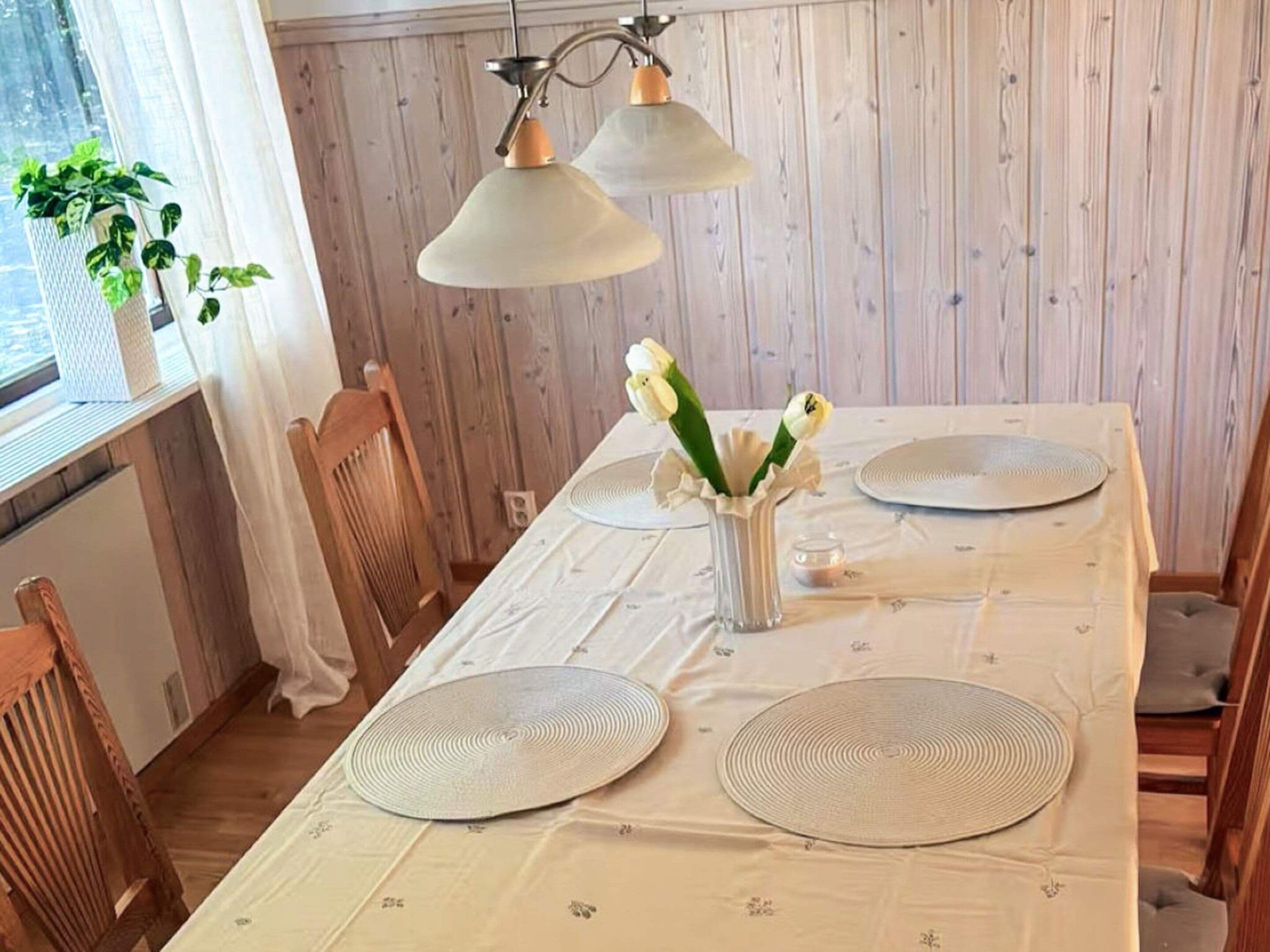 A dining table set with placemats, a vase with flowers, and a hanging light fixture.