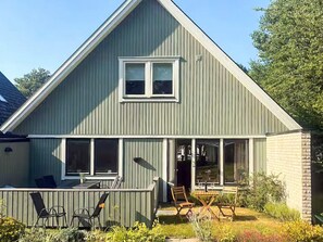 A two-story house with a sloped roof, a front porch with chairs, and a small garden area. - 5 Person Holiday Home in Brakne-hoby (Brakne-Hoby)
