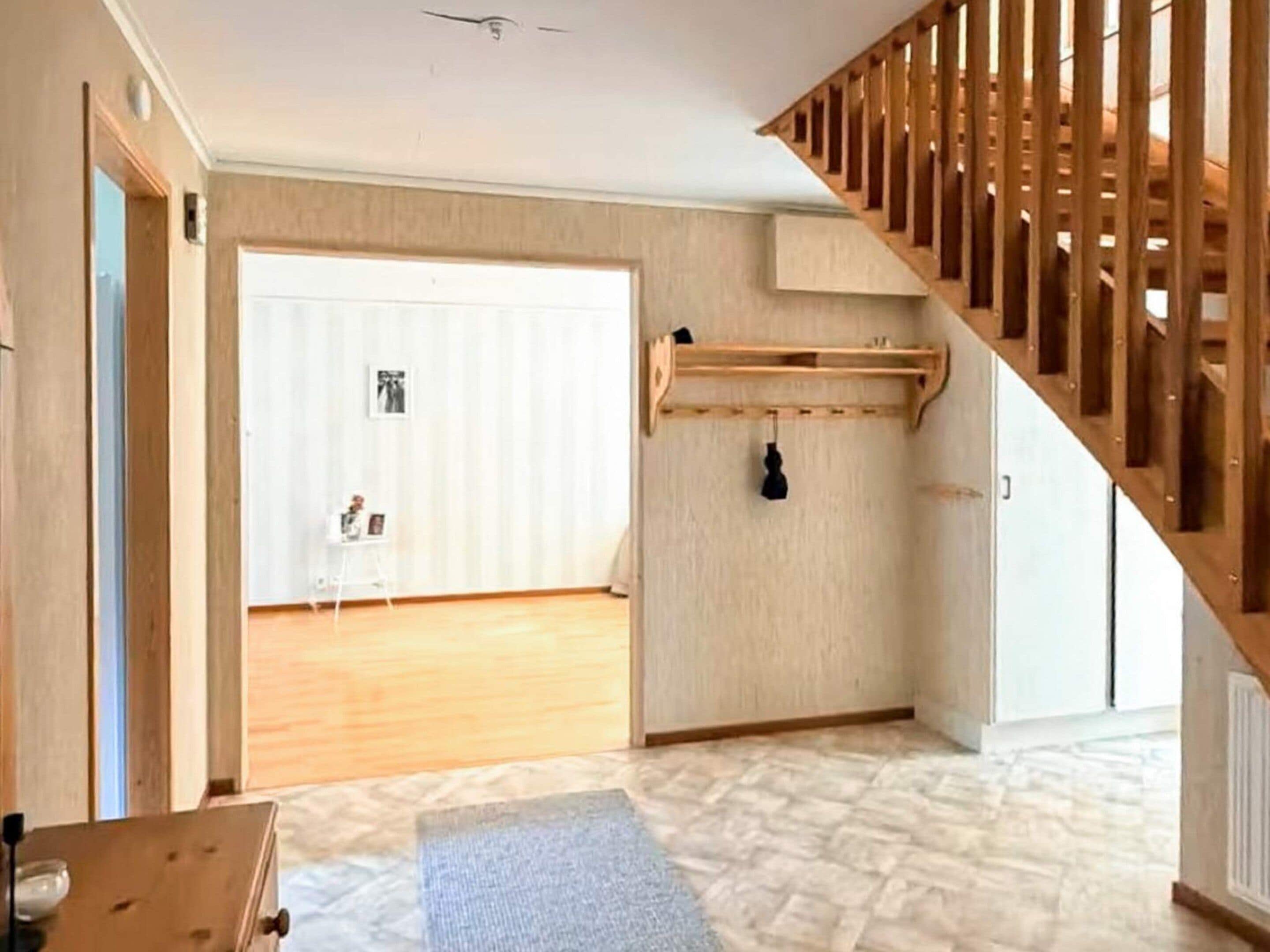 Una habitación con escalera de madera, una puerta blanca y una pequeña mesa con un tapete.