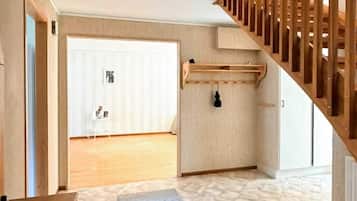 Una habitación con escalera de madera, una puerta blanca y una pequeña mesa con un tapete.