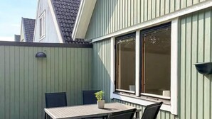 Eine Terrasse mit Tisch, Stühlen, einer Kübelpflanze und einem Fenster mit Jalousien.