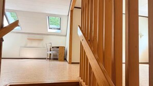 Eine Holztreppe führt zu einem Raum mit einem weißen Heizkörper, einem Stuhl und einem Fenster.