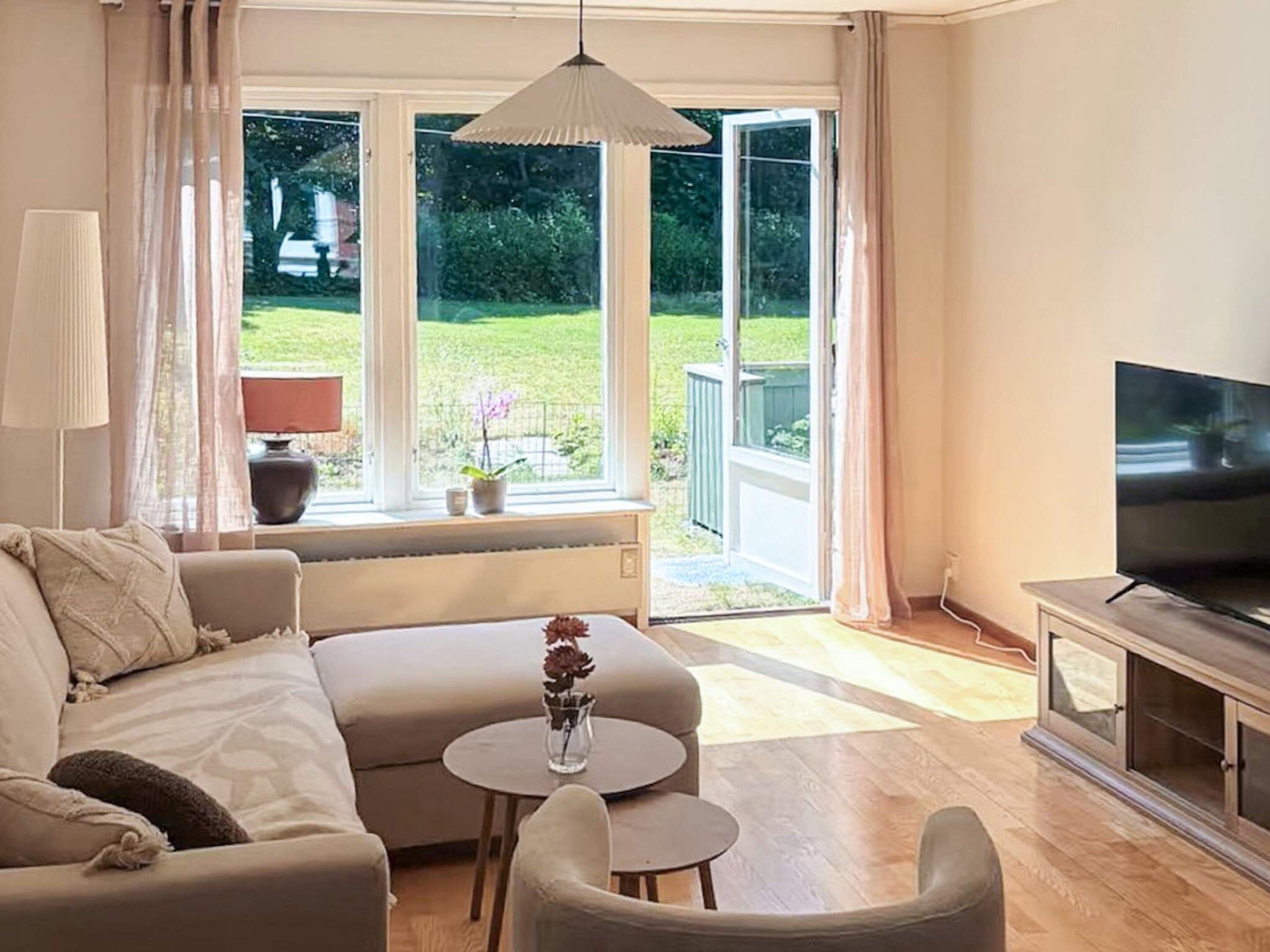 Un salon comprenant un canapé, deux petites tables, un téléviseur et une porte-fenêtre coulissante donnant sur un jardin.