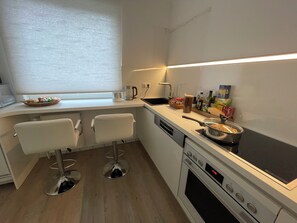 A modern kitchen with a built-in oven, a stovetop, and a window with blinds. - Two rooms with a balcony (Borgholzhausen)