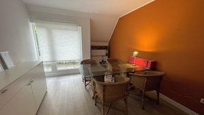 Un interior moderno con una mesa de comedor de vidrio, sillas de mimbre, un armario blanco y una lámpara roja en la pared.