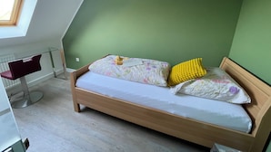 Una habitación con techo inclinado, una cama con ropa de cama floral, un almohadón amarillo y un escritorio con una silla.