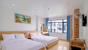 Habitación de hotel con dos camas, un cuadro en la pared, una ventana con cortinas y una mesita de noche de madera con un control remoto.