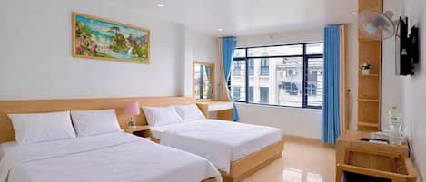 Camera d'albergo con due letti, un quadro appeso al muro, una finestra con tende e un comodino in legno con un telecomando.