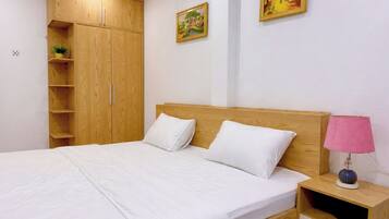 A bedroom with a bed, wooden wardrobe, two paintings, and a bedside lamp.