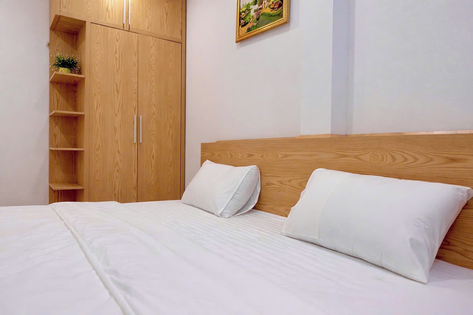 Une chambre avec une armoire en bois, un lit avec une literie blanche et un tableau accroché au mur.