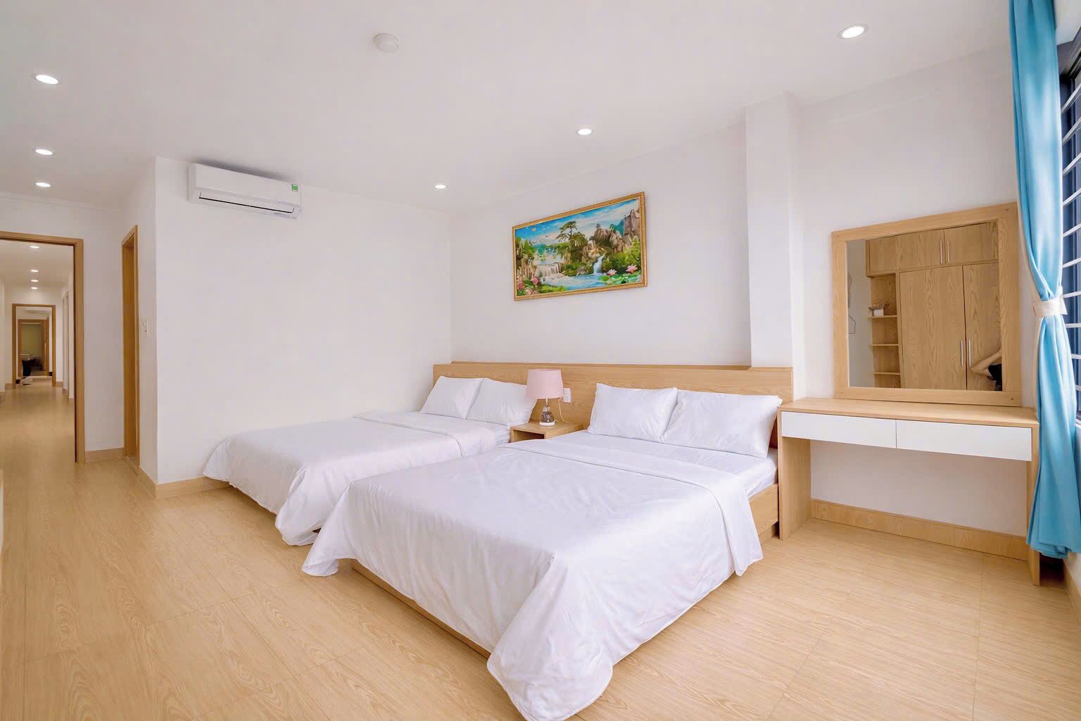 A hotel room with two beds, a painting, a mirror, and a wooden wardrobe.