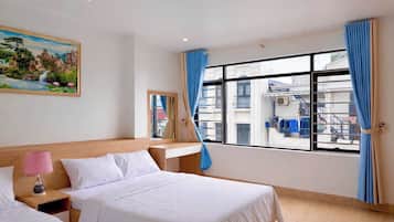 A hotel room with two beds, a large window with curtains, a painting on the wall, and a view of the outside.