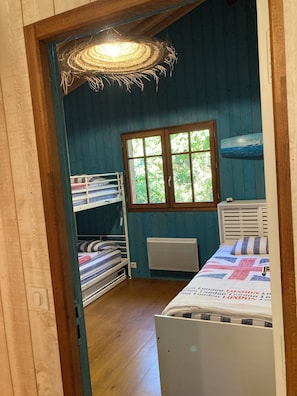 Ein Zimmer mit Etagenbetten, einem Heizkörper, einem Fenster mit Blick auf Grünflächen und einem an der Wand befestigten Regal mit einem Gemälde.