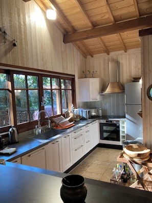 Eine Küche mit Holzwänden, einem großen Fenster und modernen Geräten, darunter ein Herd, ein Backofen und ein Kühlschrank.