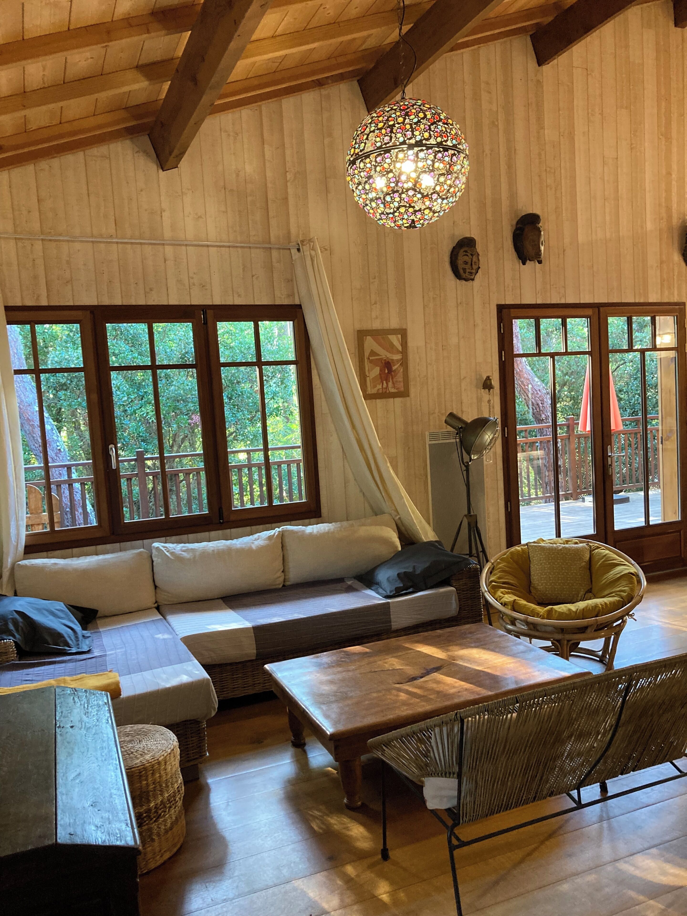 Una habitación acogedora con techo de madera, ventanas grandes, un sofá, un sillón y una mesa.