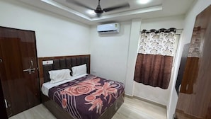 A bedroom with a bed, a ceiling fan, an air conditioning unit, and a window with curtains. - Om Home Stay (Agra)